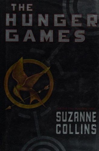 Cover of a paperback edition of The Hunger Games by Suzanne Collins, showing a golden mockingjay pin on a dark background